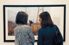 2 people look at a photograph of pylons and birdwatchers in the gallery.